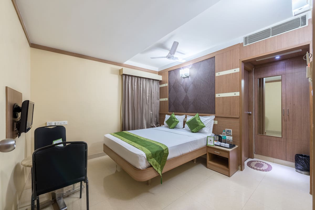 Una habitación de hotel con cama, escritorio, silla, armario y ventilador de techo.