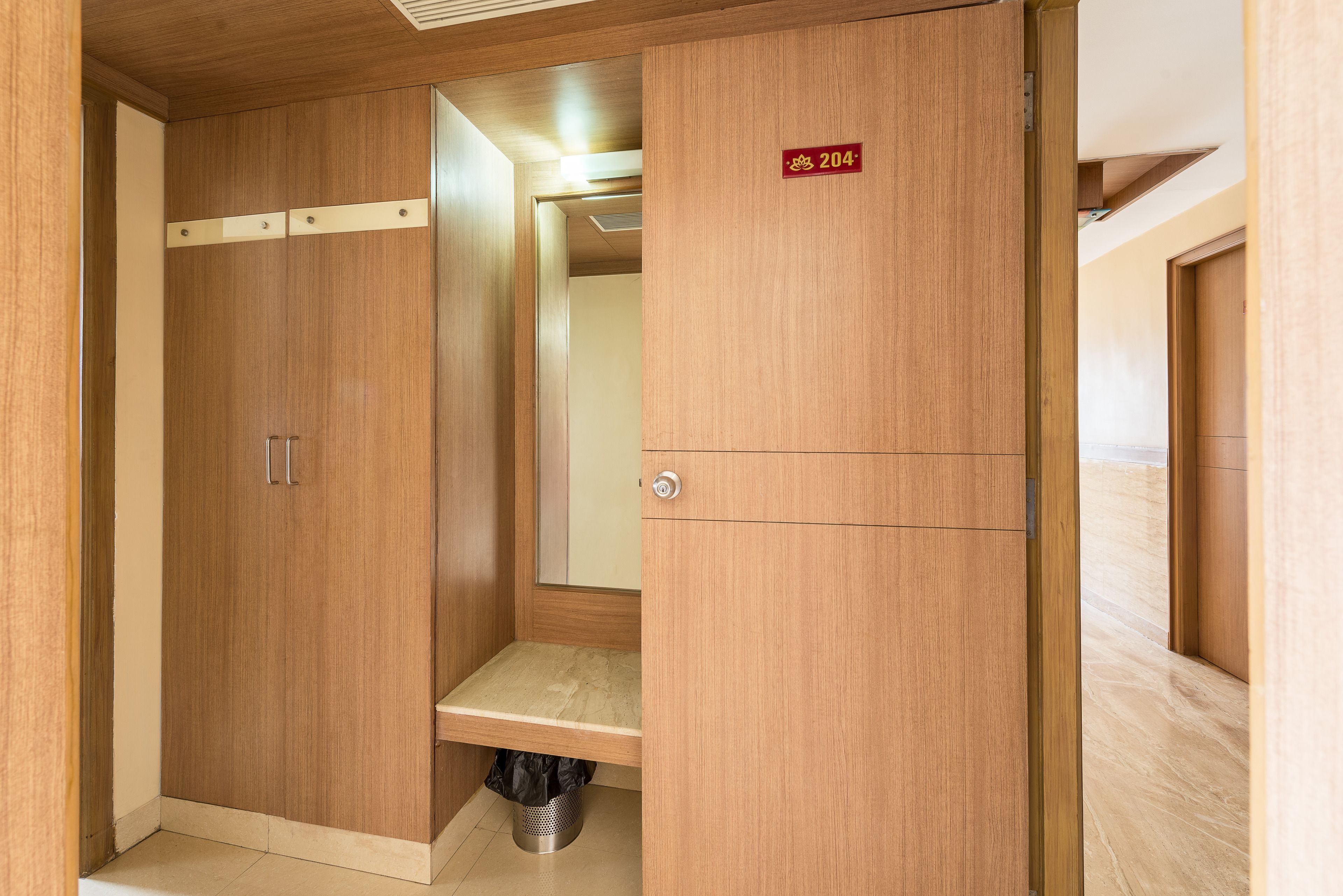 A wooden wardrobe with a mirror, a shelf, and a trash bin.