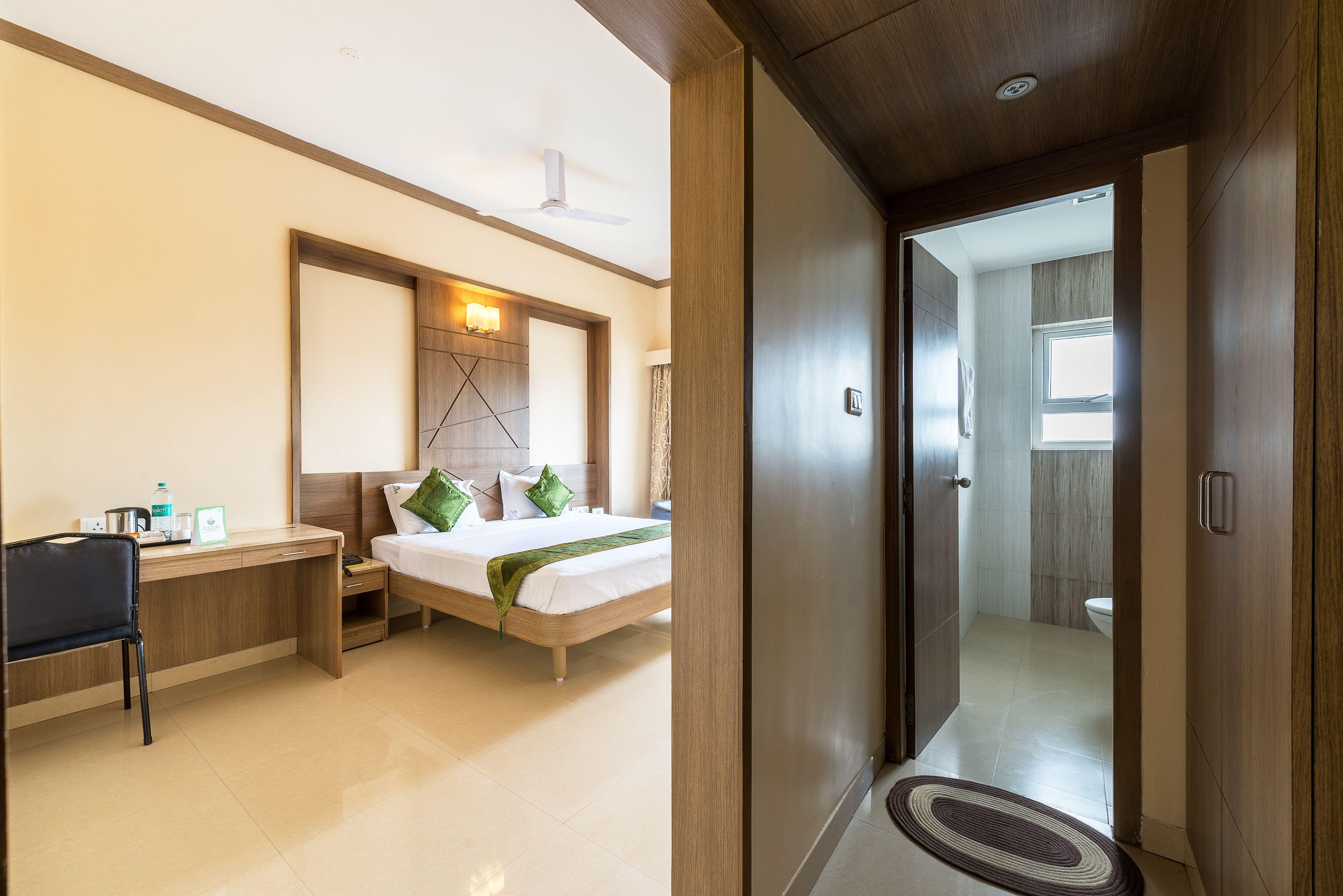 Habitación de hotel con cama, escritorio, silla y un baño visible a través de una puerta abierta.