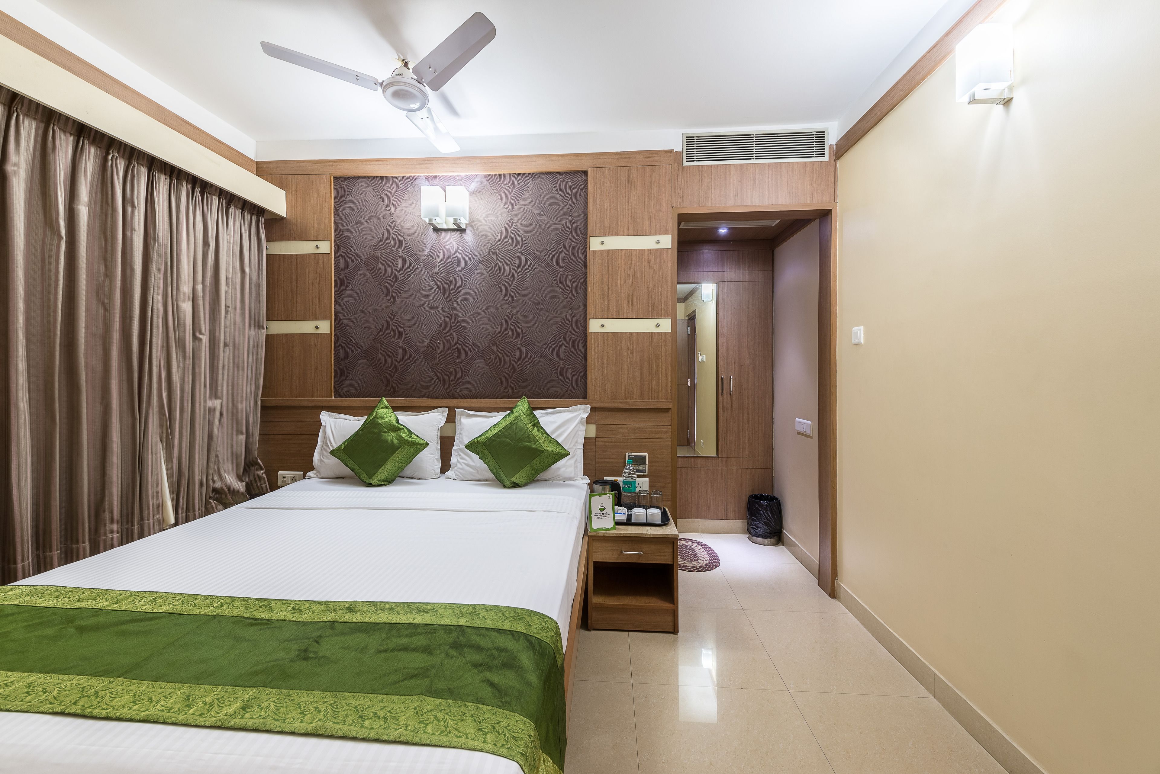 Une chambre d’hôtel comprenant un lit, une table de chevet, un ventilateur de plafond, un miroir et une porte donnant sur une autre pièce.