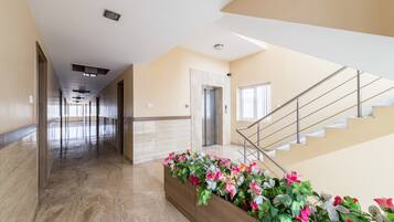 A modern hotel lobby with a marble floor, a wooden reception desk, and a staircase.