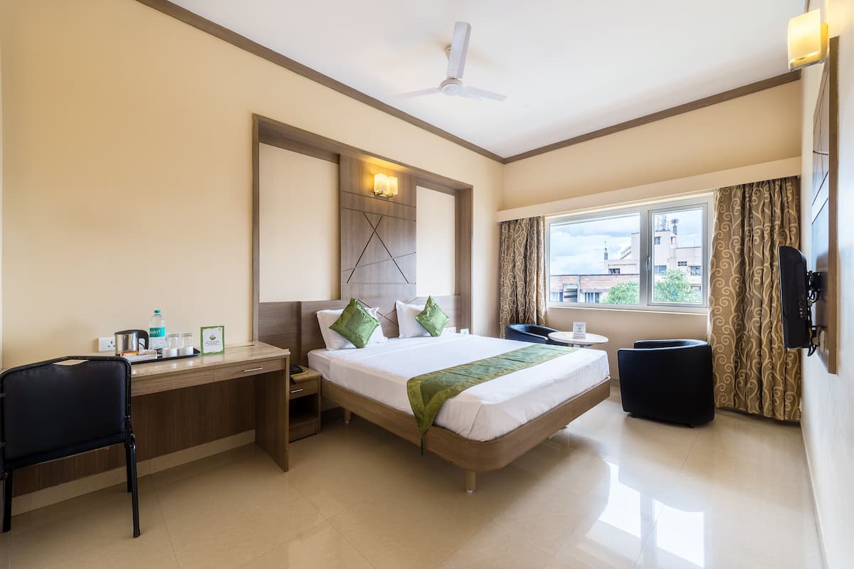 Habitación de hotel con cama, escritorio, silla, mesita de noche y televisor.