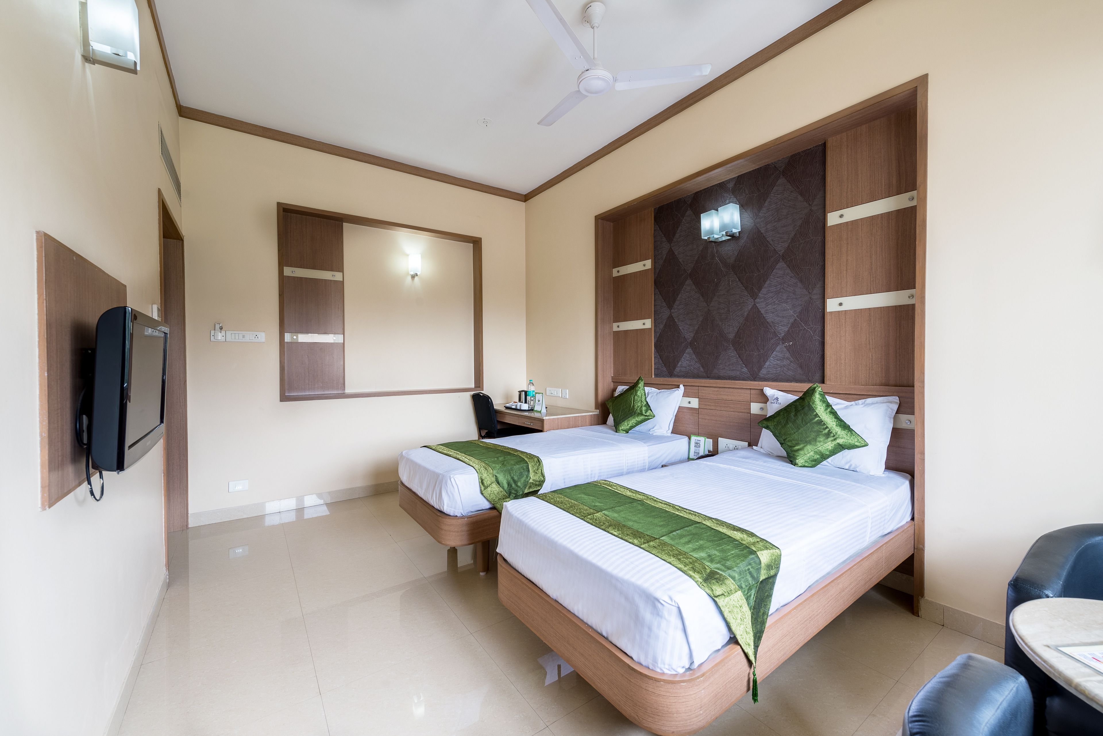 A hotel room with two beds, a desk, a chair, a TV, and a ceiling fan.