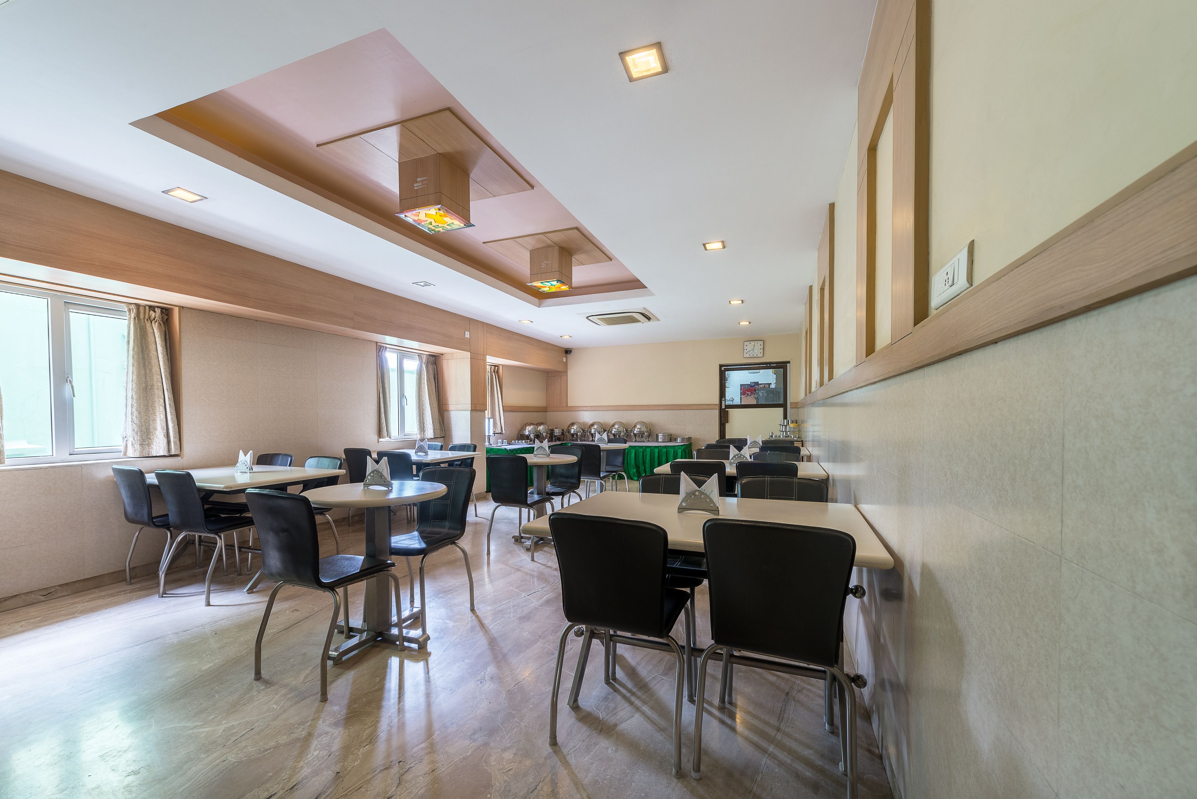 A modern dining area with multiple tables and chairs, large windows, and a ceiling with recessed lighting.