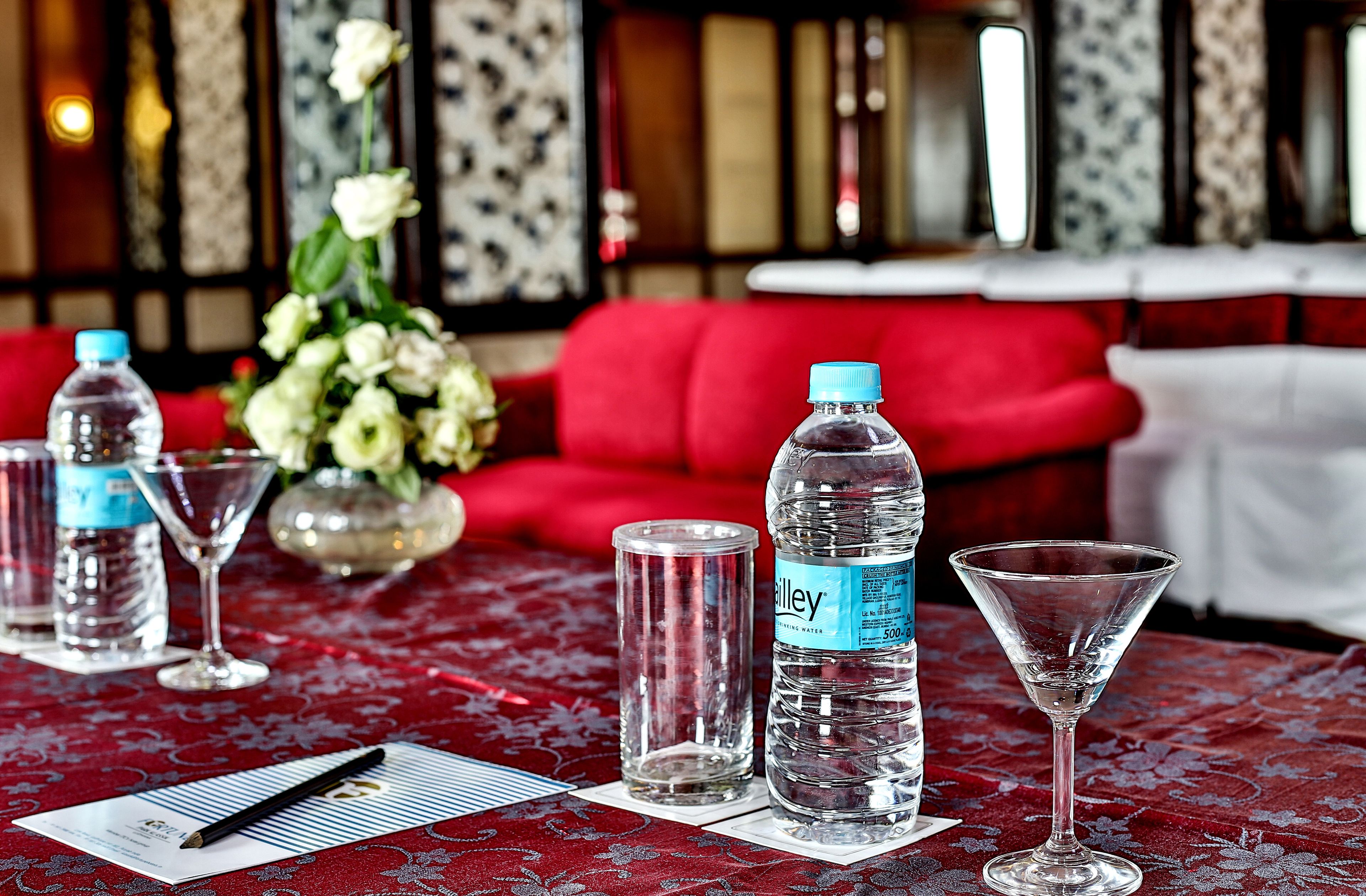 A table with water bottles, a pen, and glasses on a red patterned tablecloth.
