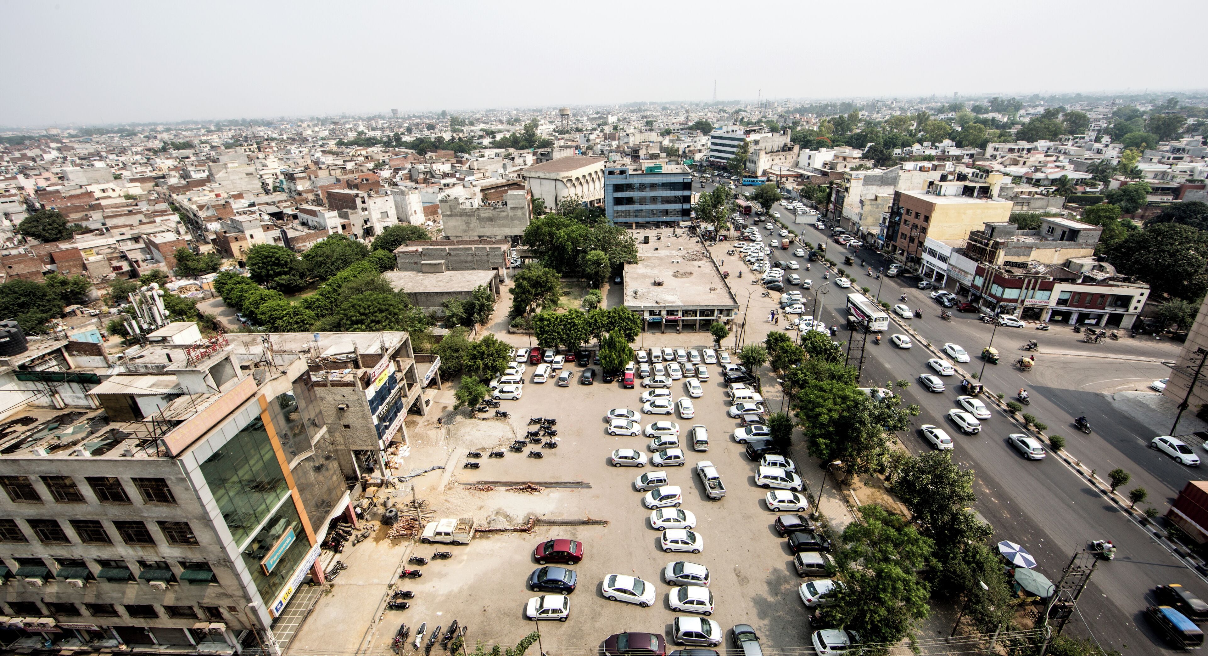 An aerial view of a densely populated urban area with numerous buildings, a large parking lot, and busy streets.