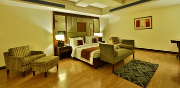 Una habitación de hotel con una cama, dos sillones, una mesita de noche, una lámpara y una alfombra estampada.