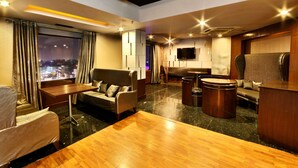 A modern hotel room with a wooden floor, a sofa, a table, and a TV mounted on the wall. - Regenta Central Klassik (Ludhiana)