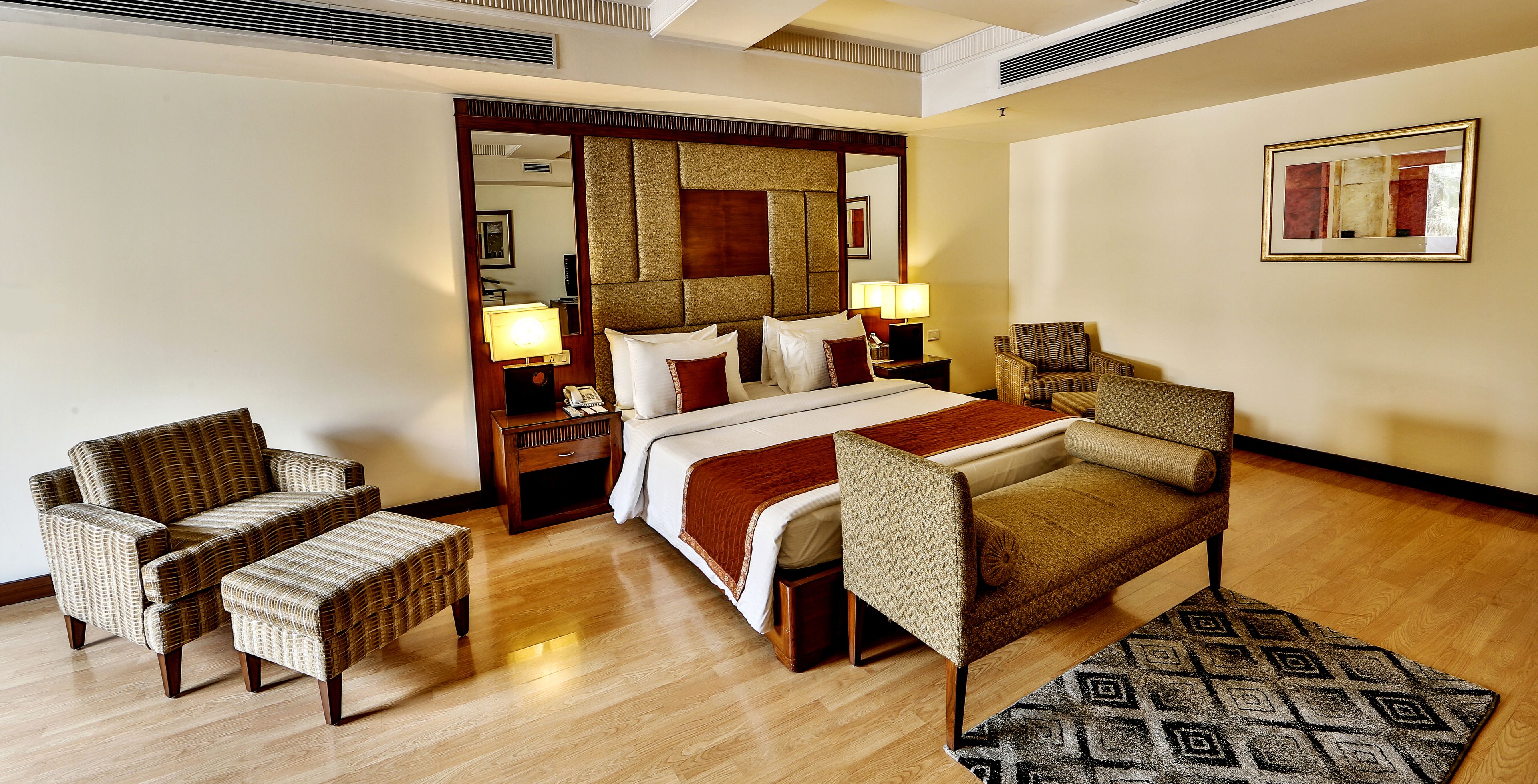 A hotel room with a bed, two armchairs, a small table, a nightstand, and a mirror.