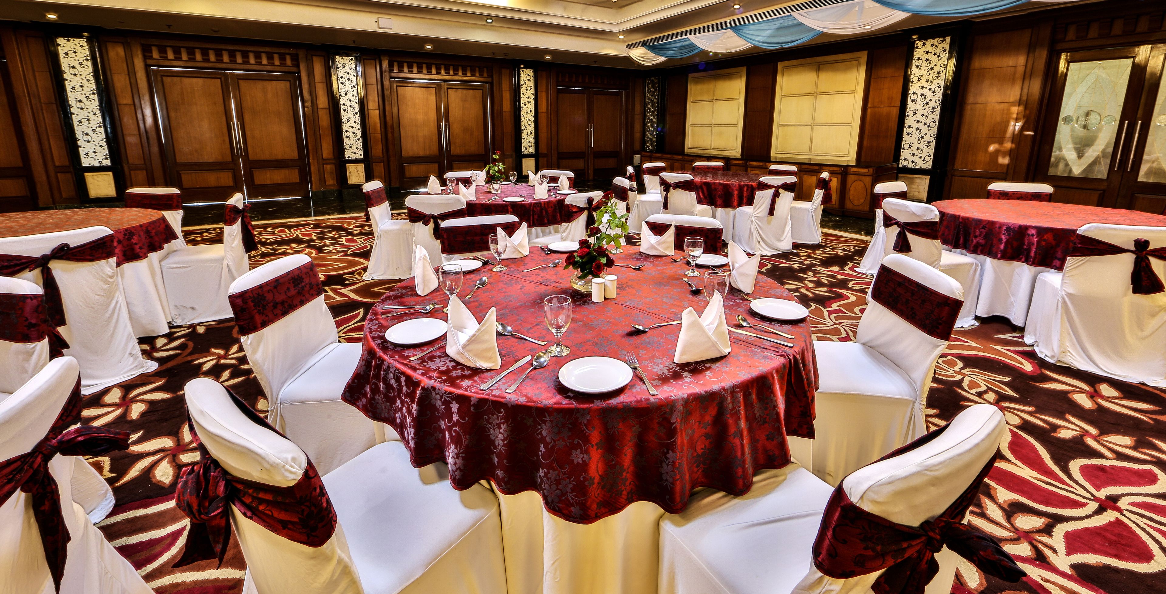 Une salle de banquet avec des tables rondes, des chaises blanches et des nappes rouges.