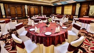 Une salle de banquet avec des tables rondes, des chaises blanches et des nappes rouges.