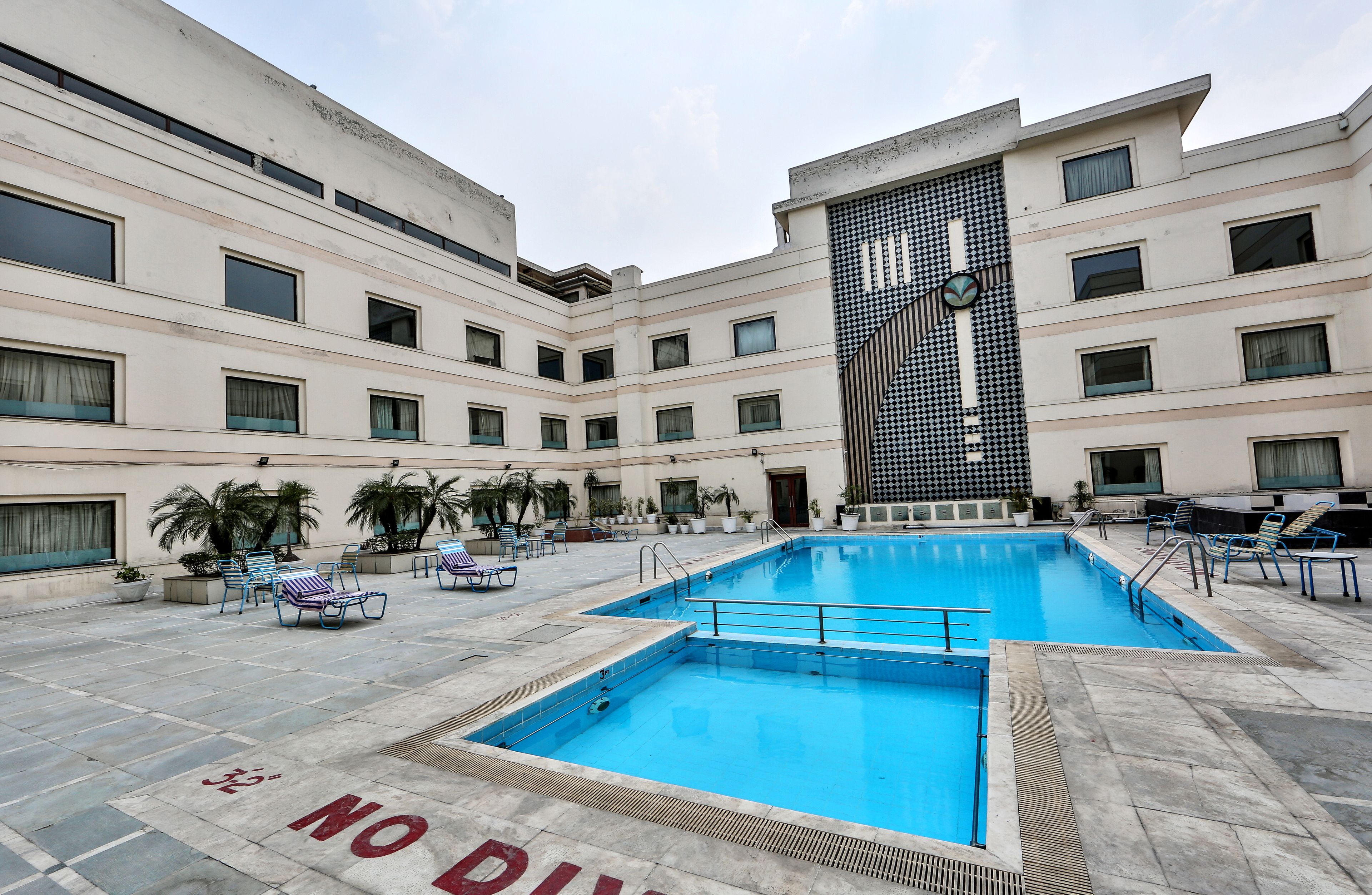 Une cour d’hôtel dotée d’une piscine, de chaises longues et d’une façade de bâtiment remarquable.