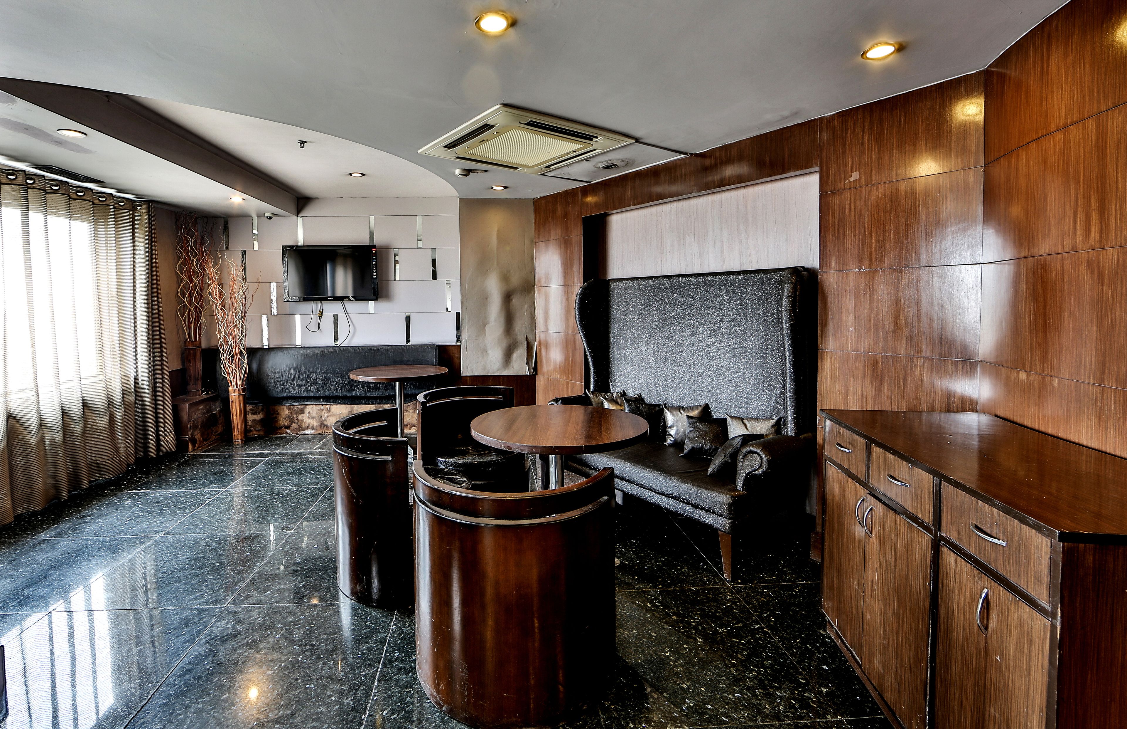 Een modern interieur met een bank, twee ronde tafels en een aan de muur bevestigde televisie.