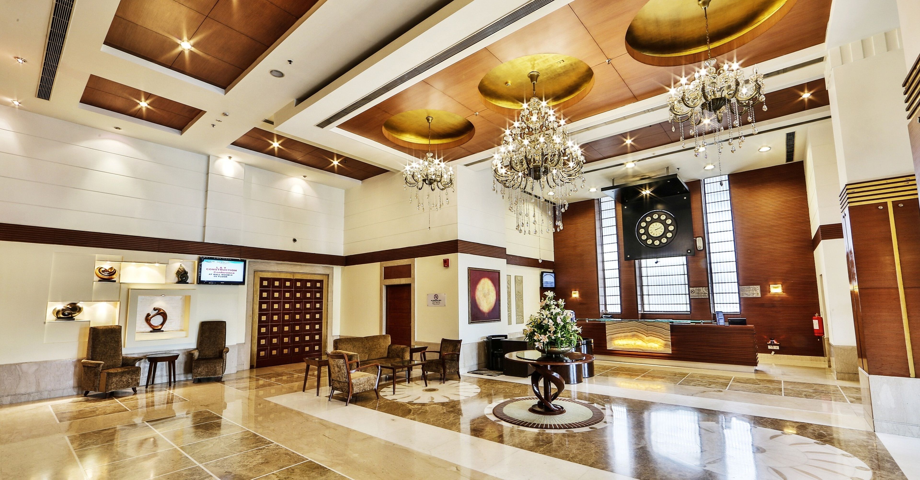 Un hall d’entrée spacieux avec un plafond haut, des lustres, un comptoir de réception et une horloge au mur.
