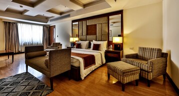 Habitación de hotel con una cama grande, dos sillones, una mesita, un escritorio y un espejo amplio.