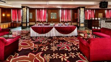 Un vestíbulo de hotel con alfombra roja, dos mesas redondas con manteles blancos, sofás rojos y un mostrador de recepción.