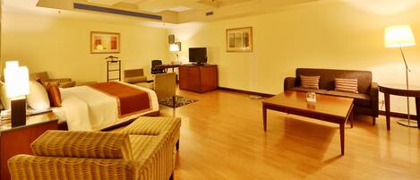 Habitación de hotel con cama, dos sillones, un sofá, una mesa de centro, televisión, escritorio y lámpara.