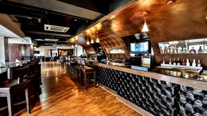 A bar area with wooden flooring, leather seating, and a bar counter with a variety of bottles. - Regenta Central Klassik (Ludhiana)