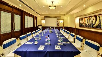 A conference room with a long table, white chairs with blue sashes, water bottles, name cards, and a projector screen.
