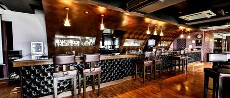 A bar with a wooden bar top, leather barstools, and pendant lighting.