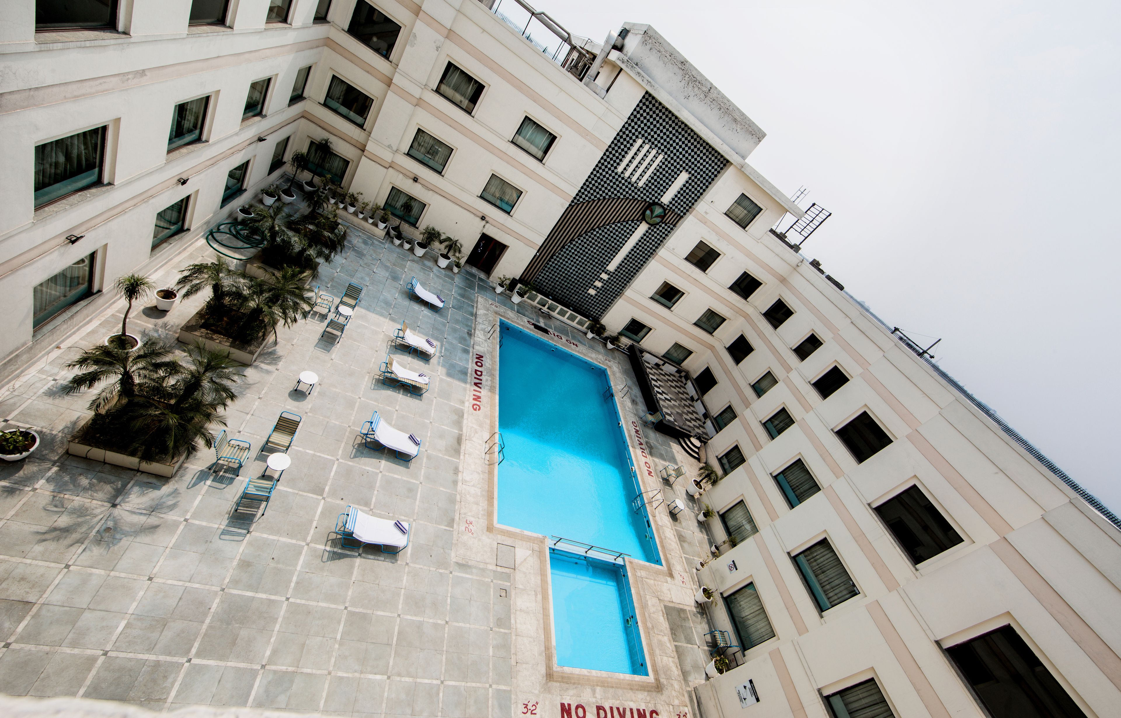 A multi-story building with a rooftop pool, outdoor seating, and palm trees.