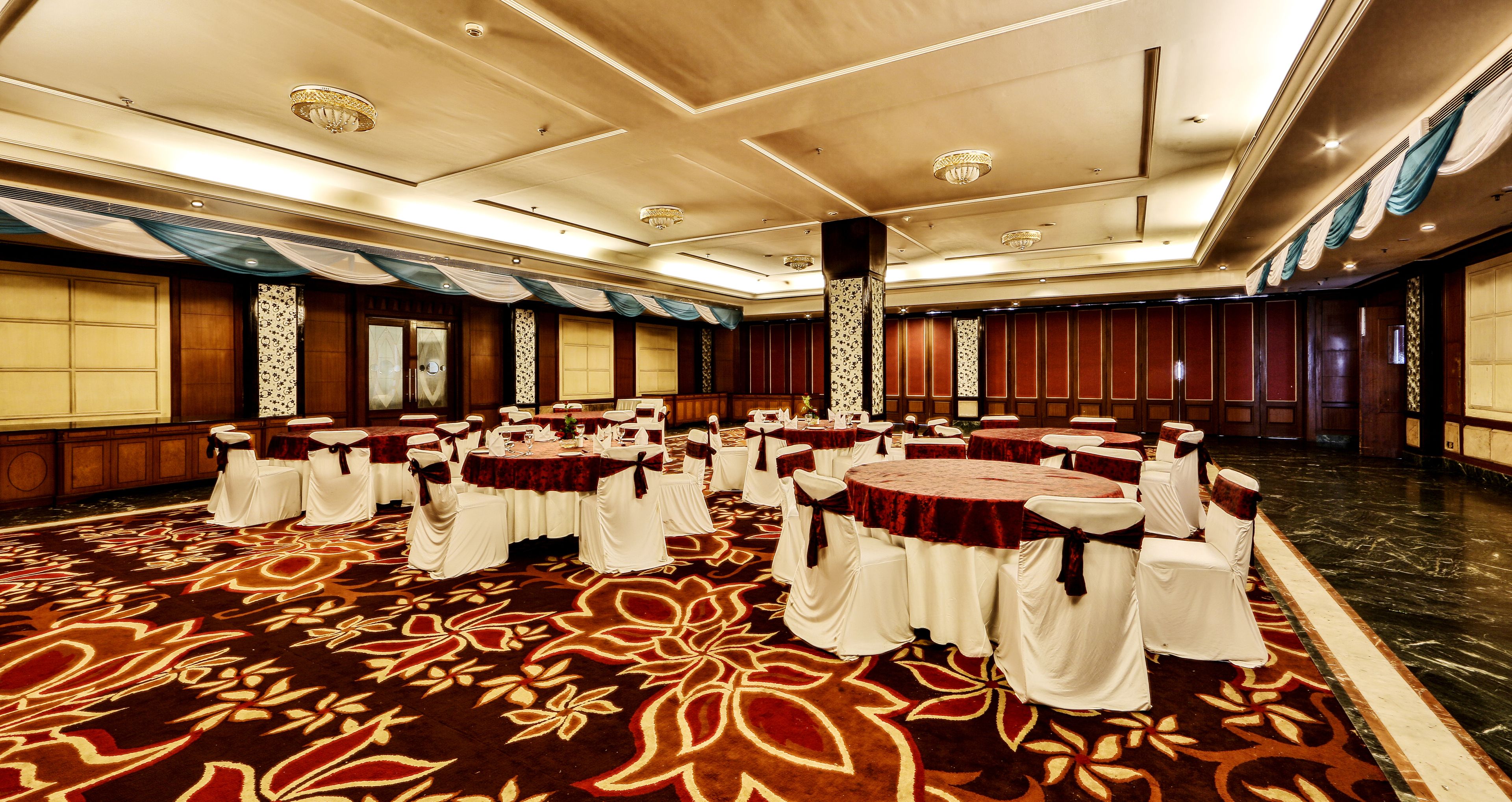 A banquet hall with round tables, white chairs, and a patterned carpet.