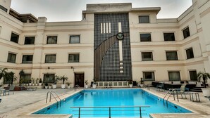 A swimming pool with a geometric wall design, surrounded by a multi-story building with balconies and potted plants. - Regenta Central Klassik (Ludhiana)