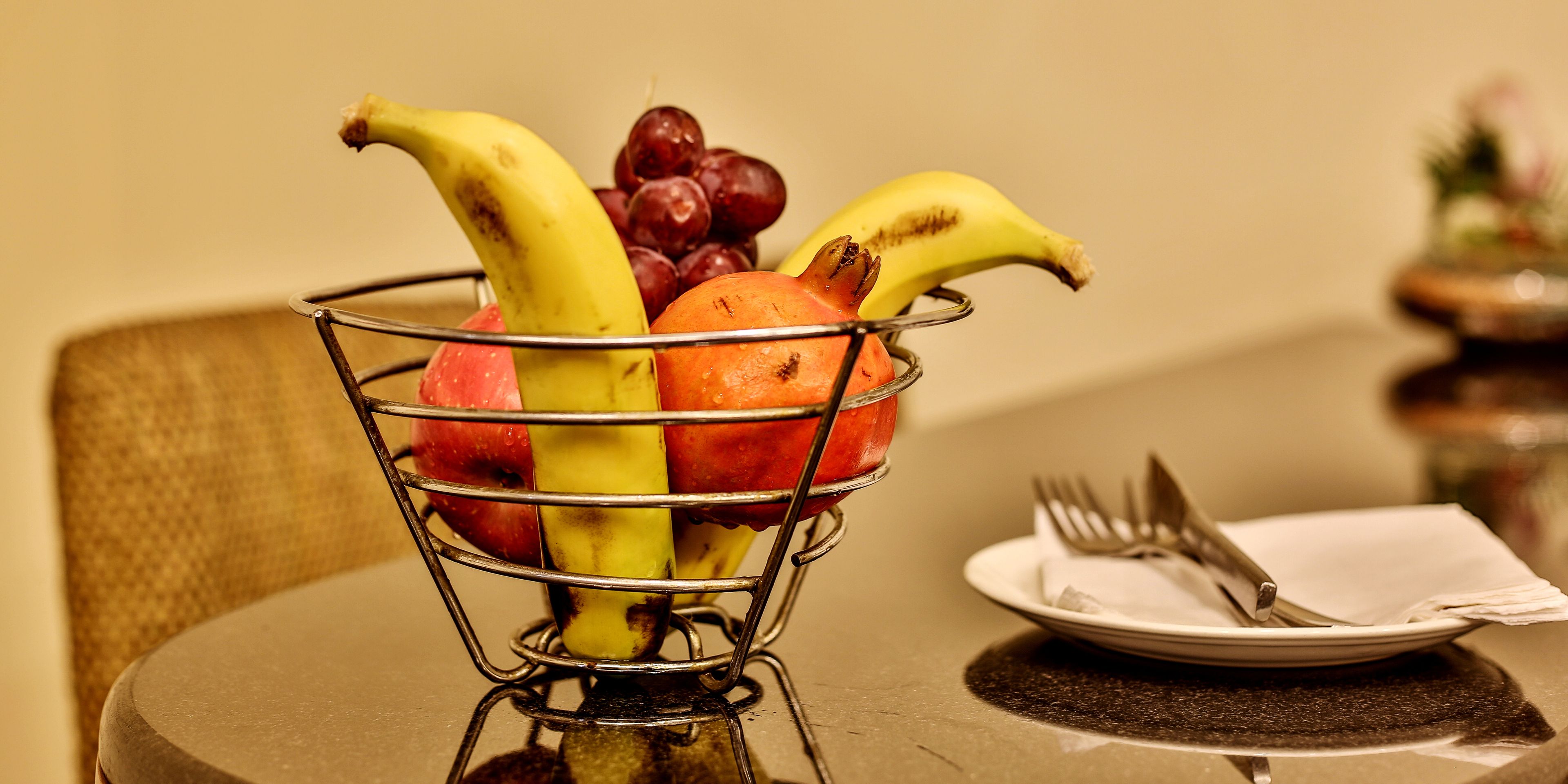 A fruit basket on a table with a plate and cutlery beside it.