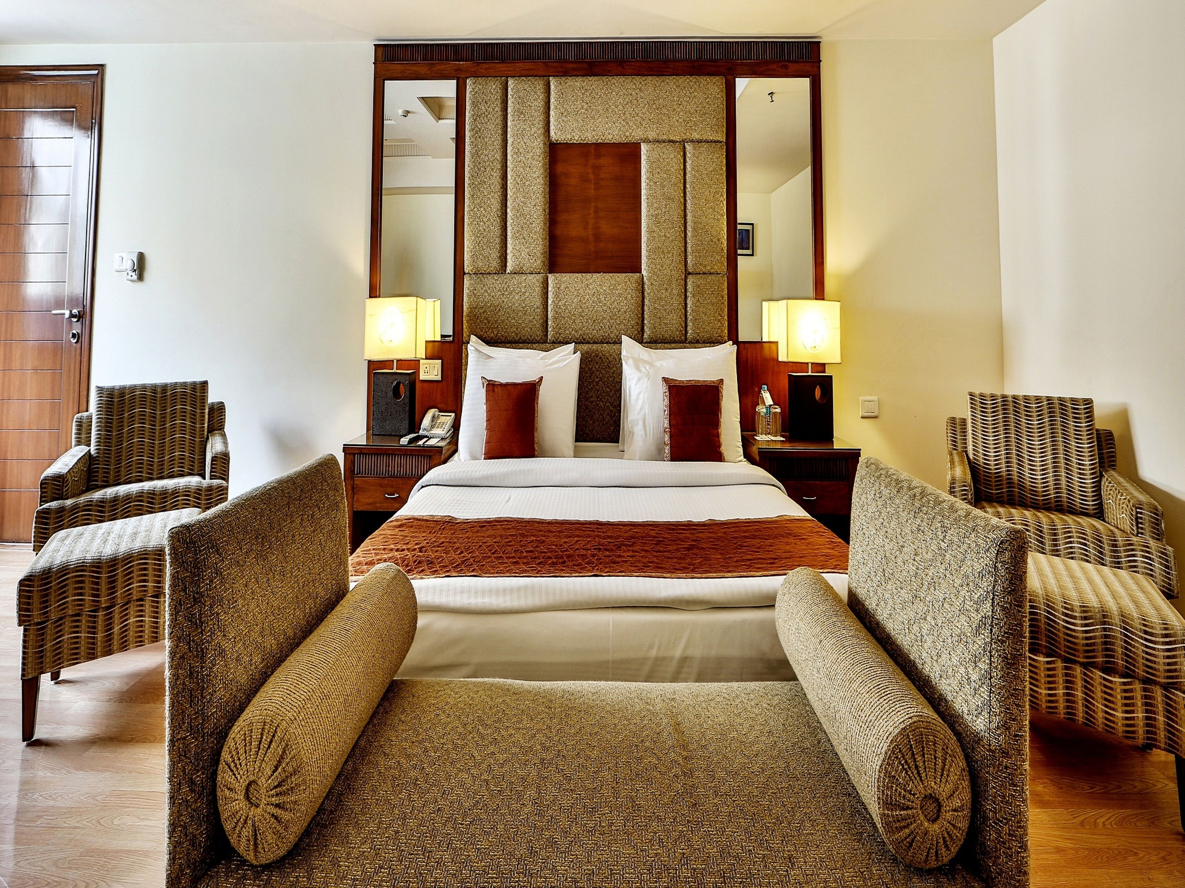 A hotel room with a large bed, two bedside tables with lamps, and four wicker armchairs.