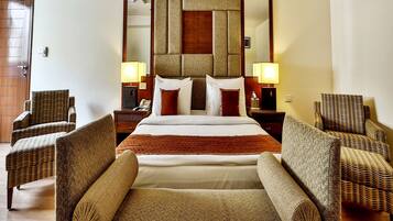 A hotel room with a large bed, two bedside tables with lamps, and four wicker armchairs.