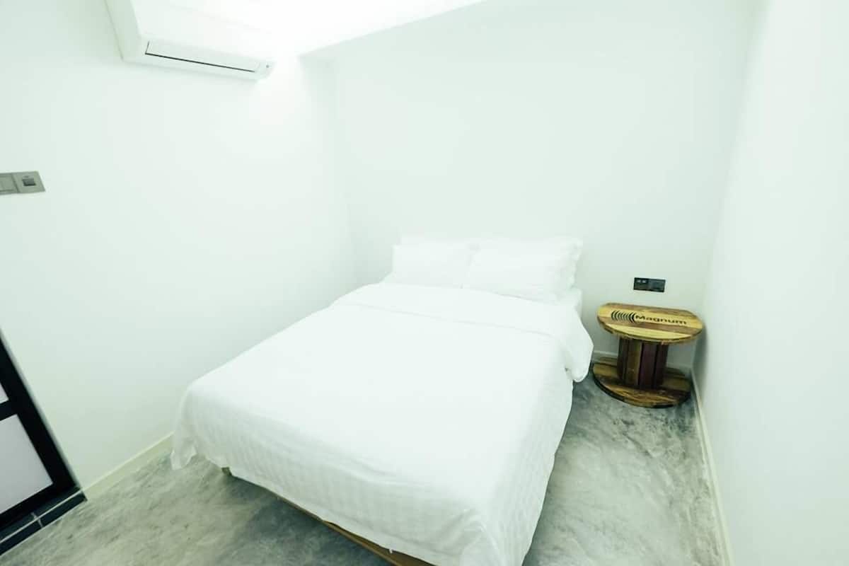 A small, white, single-bed room with a wooden side table and a small rug.
