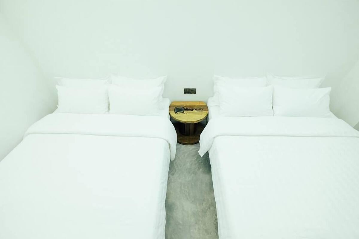 A hotel room with two single beds, a wooden nightstand with a Magnum logo, and a plain white wall.