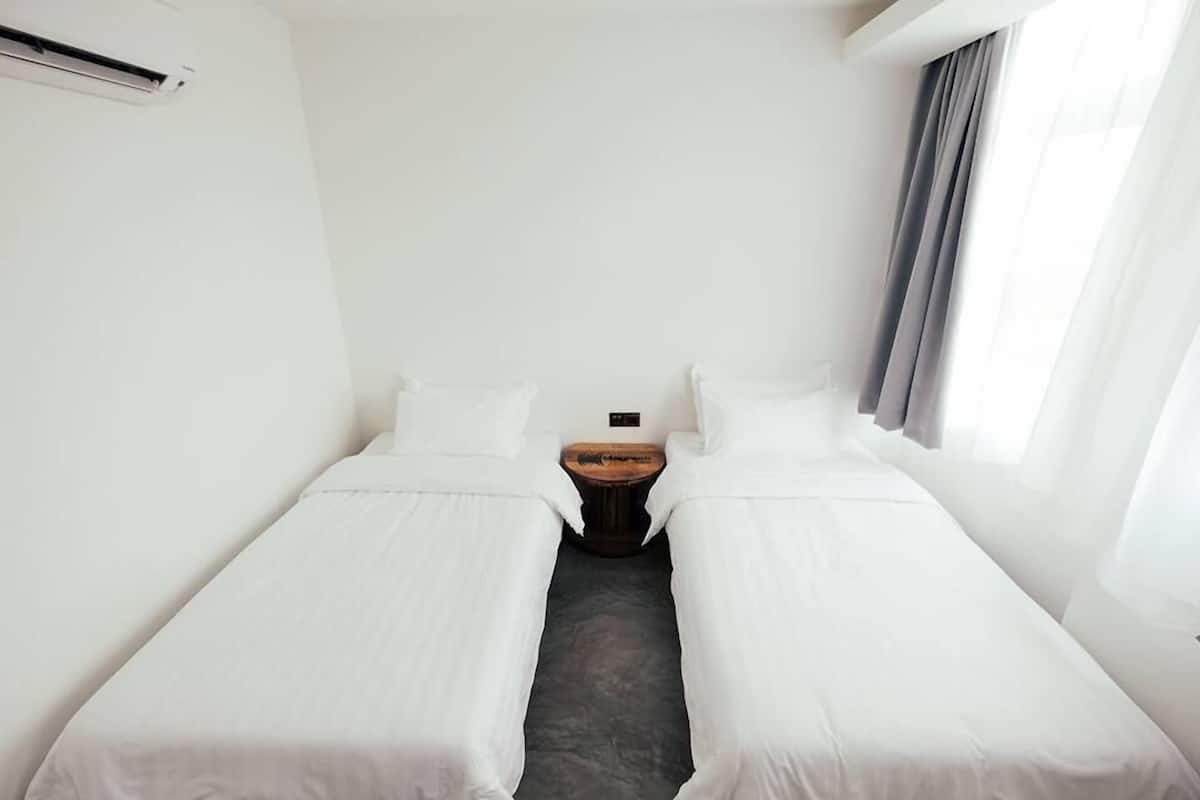 A hotel room with two single beds, a small wooden nightstand, and a window with curtains.