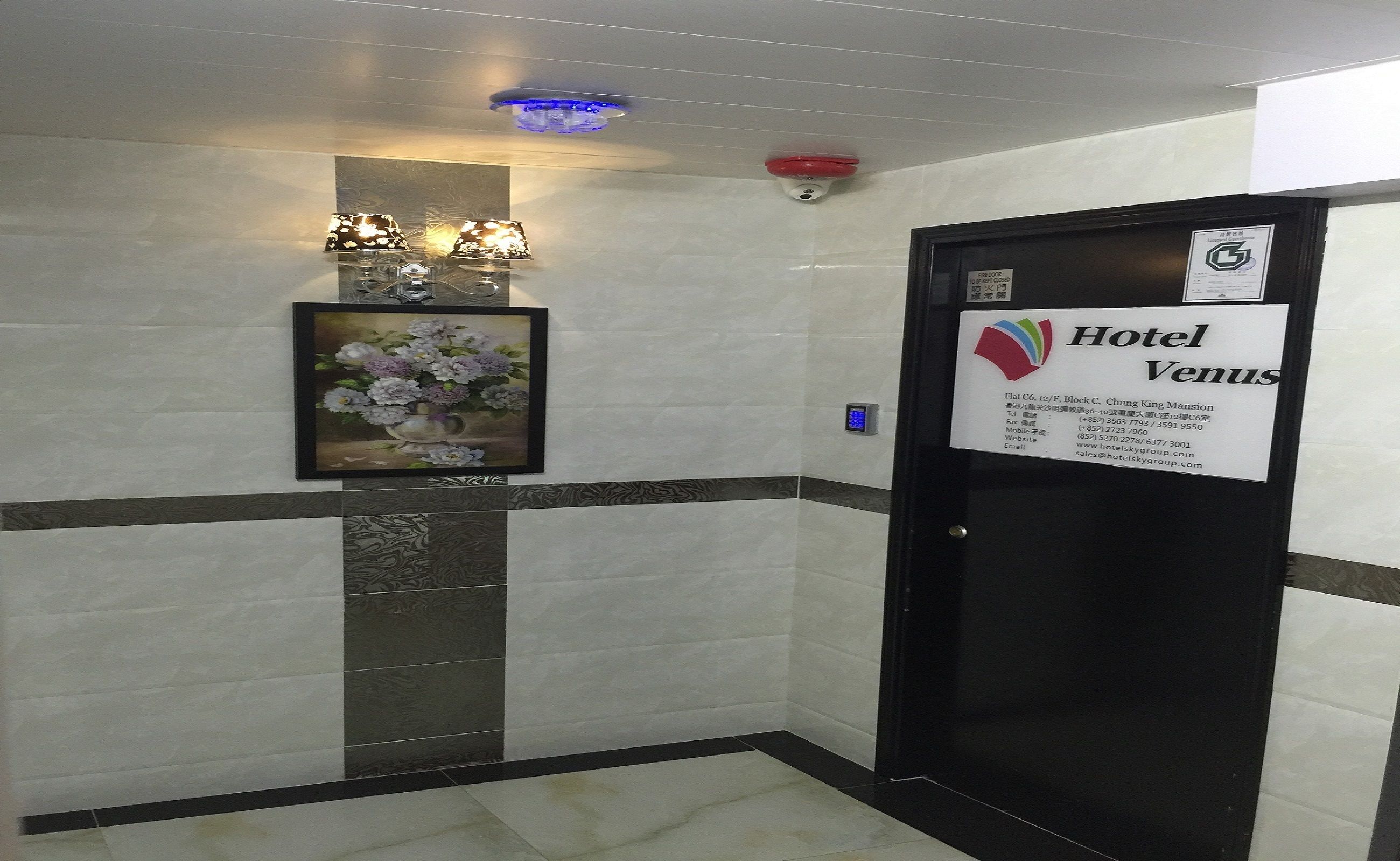 A hotel entrance with a sign for Hotel Venus, a framed floral artwork, and a fire safety sign.