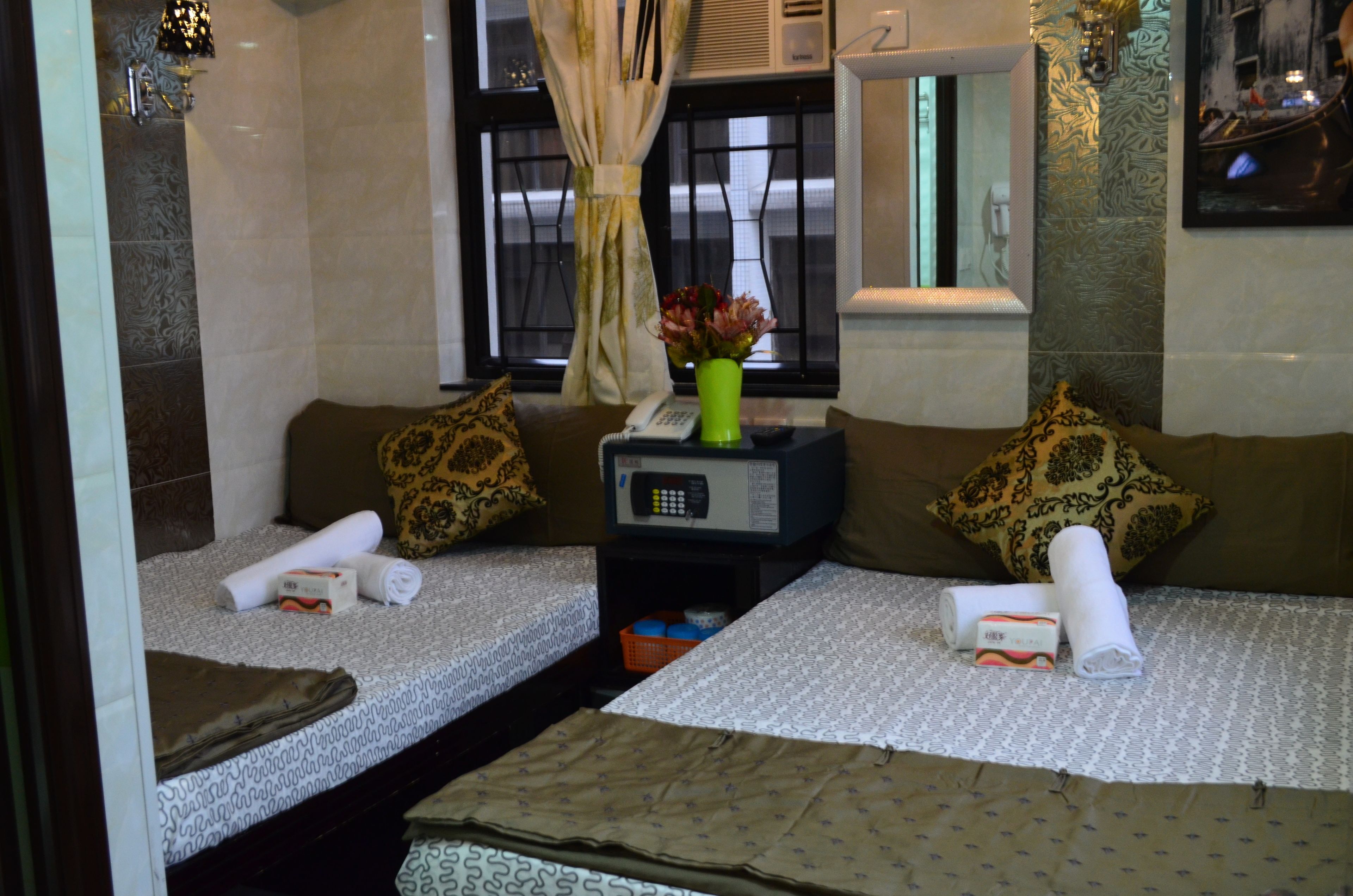 A hotel room with two beds, a small table with a telephone and a vase of flowers, and a window with curtains.