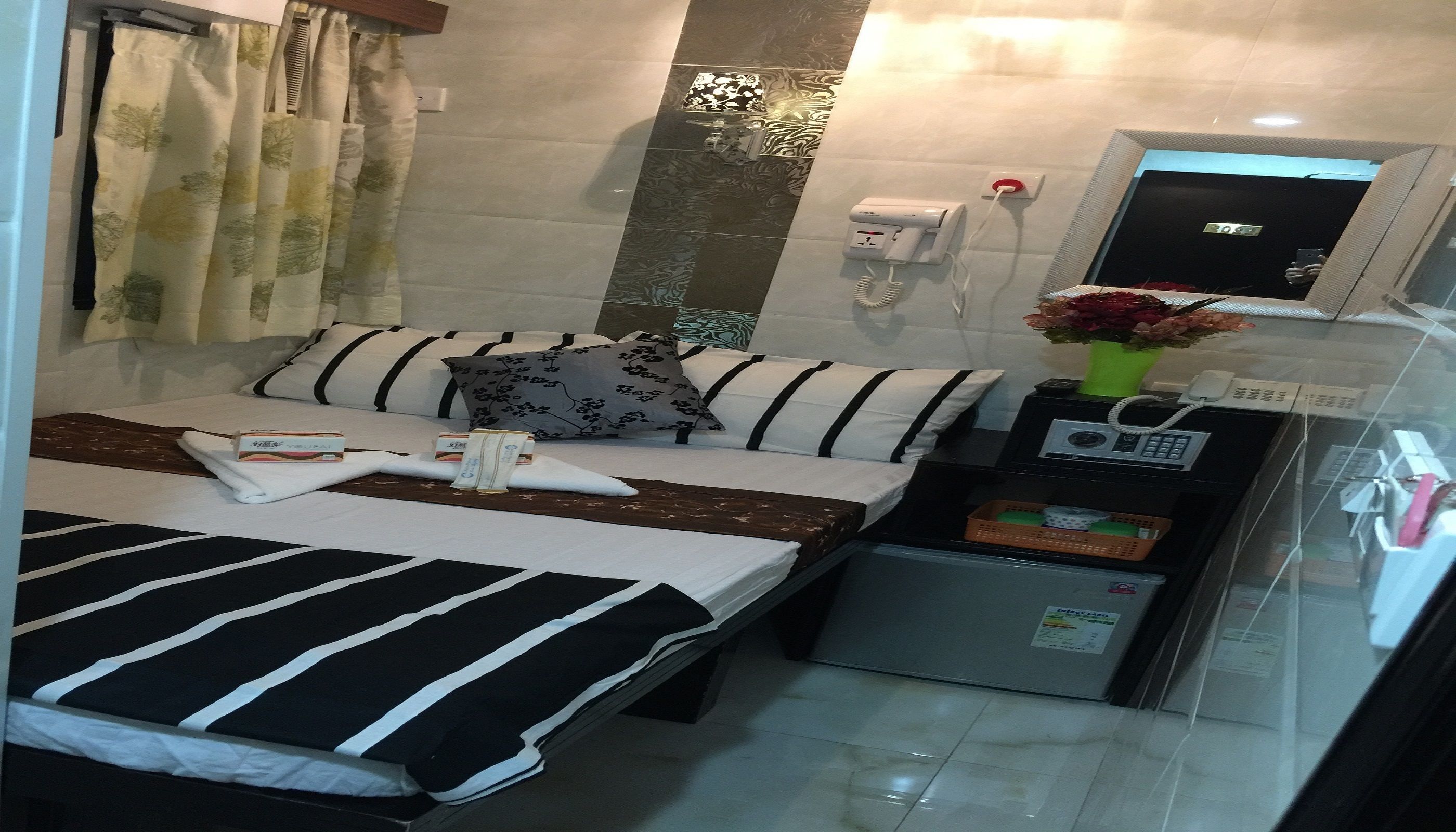 A hotel room with a bed, a small refrigerator, a telephone, and a mirror.
