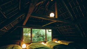 Ein gemütliches Schlafzimmer im Dachgeschoss mit schrägen Wänden, Holzbalken und einem großen Fenster mit Blick auf Grünflächen.