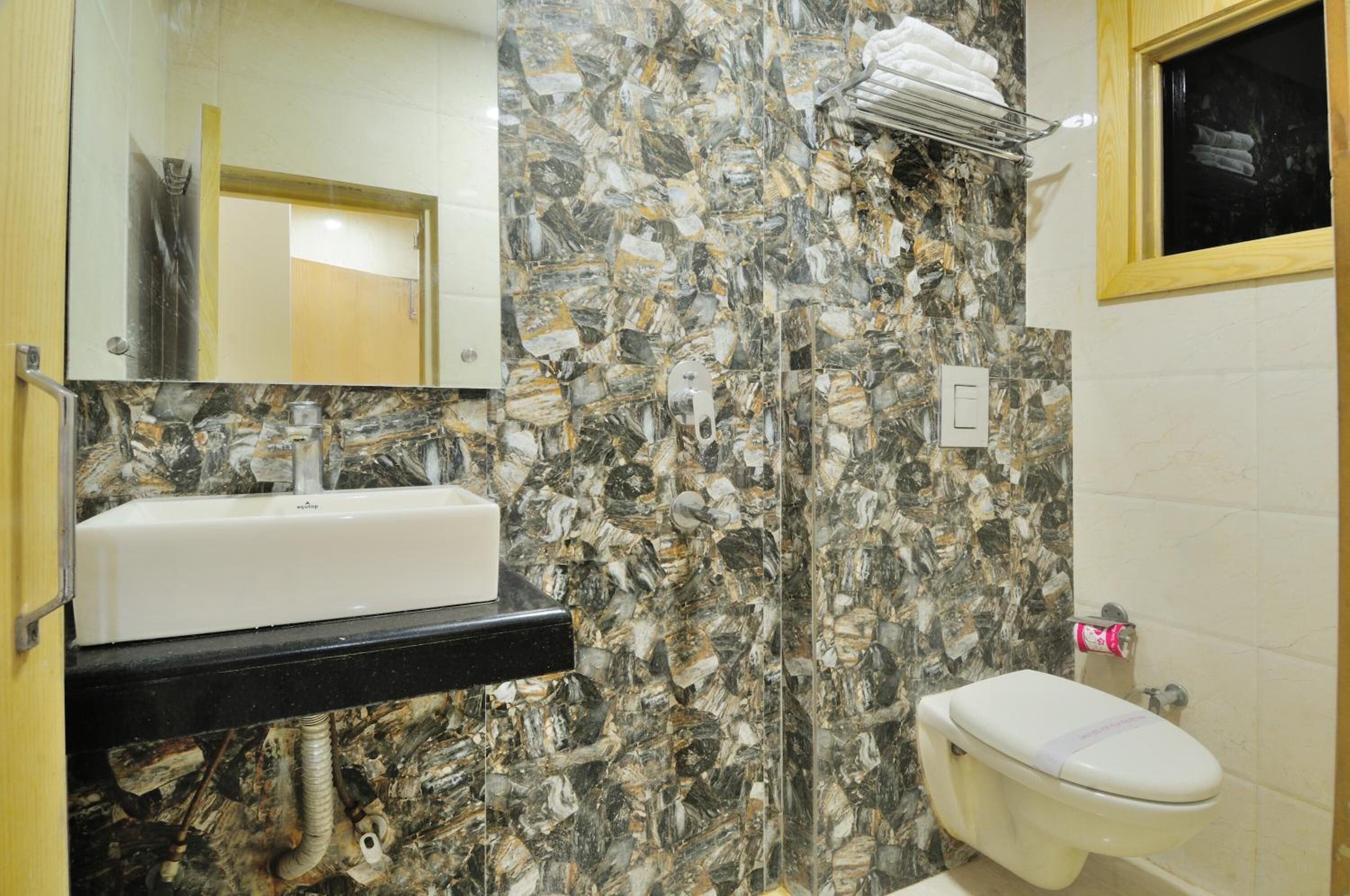 Un baño con lavamanos blanco, pared de mármol y retrete.