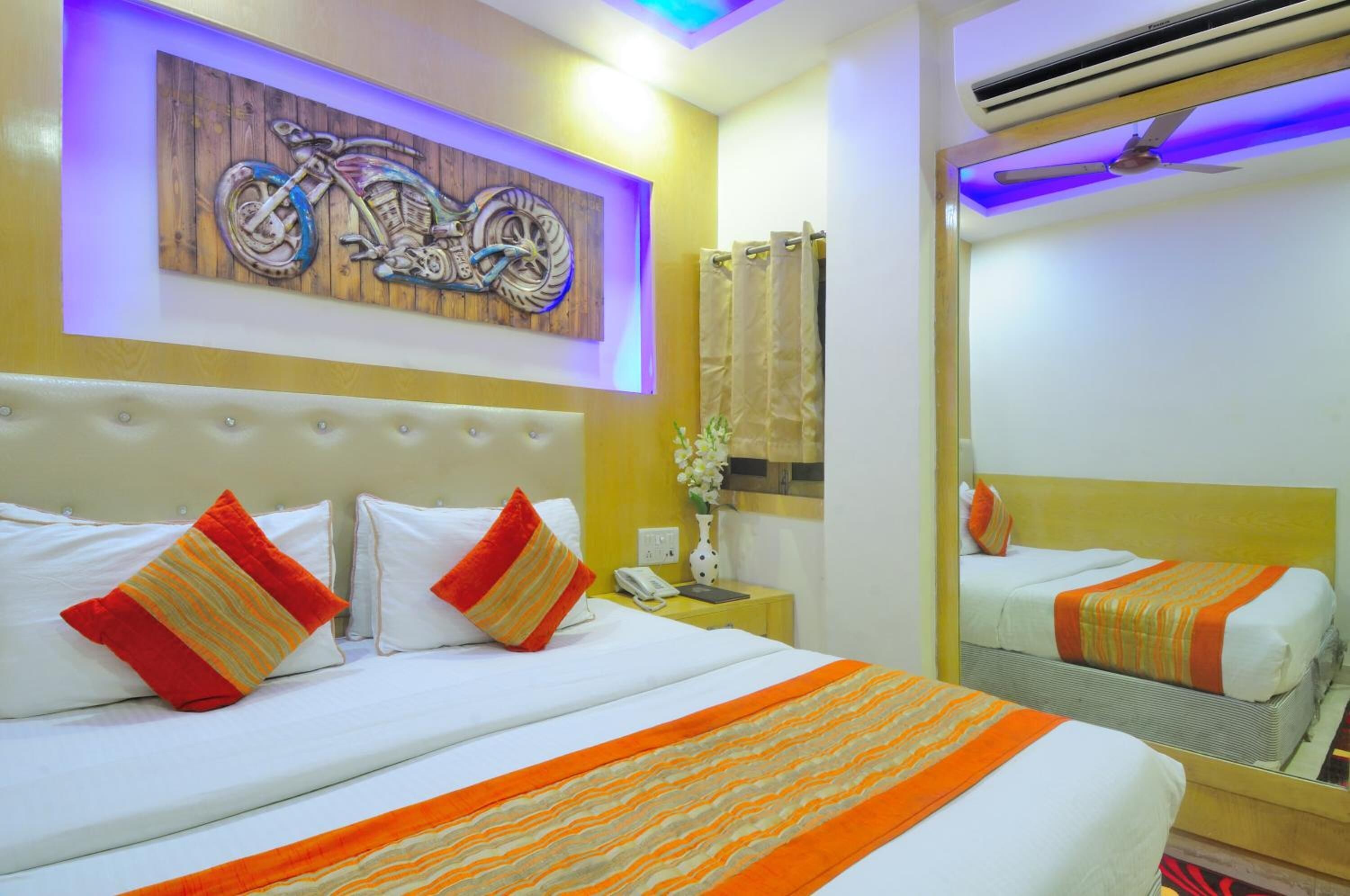 A hotel room with a large bed, a mirror, a wall-mounted artwork of a motorcycle, and a ceiling fan.