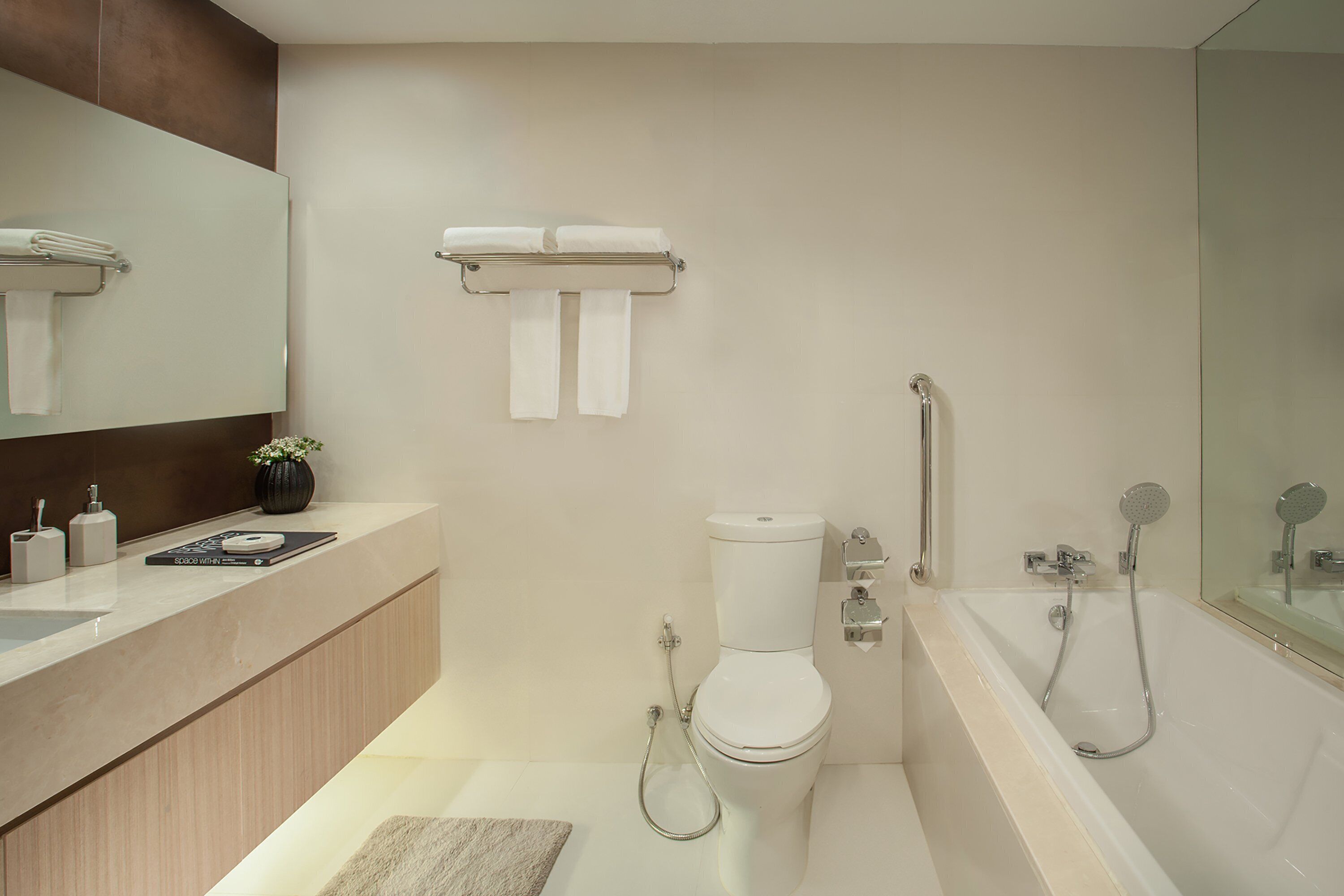 Un baño moderno con inodoro, bidé y bañera. Hay un lavamanos con espejo y un perchero sobre el inodoro.