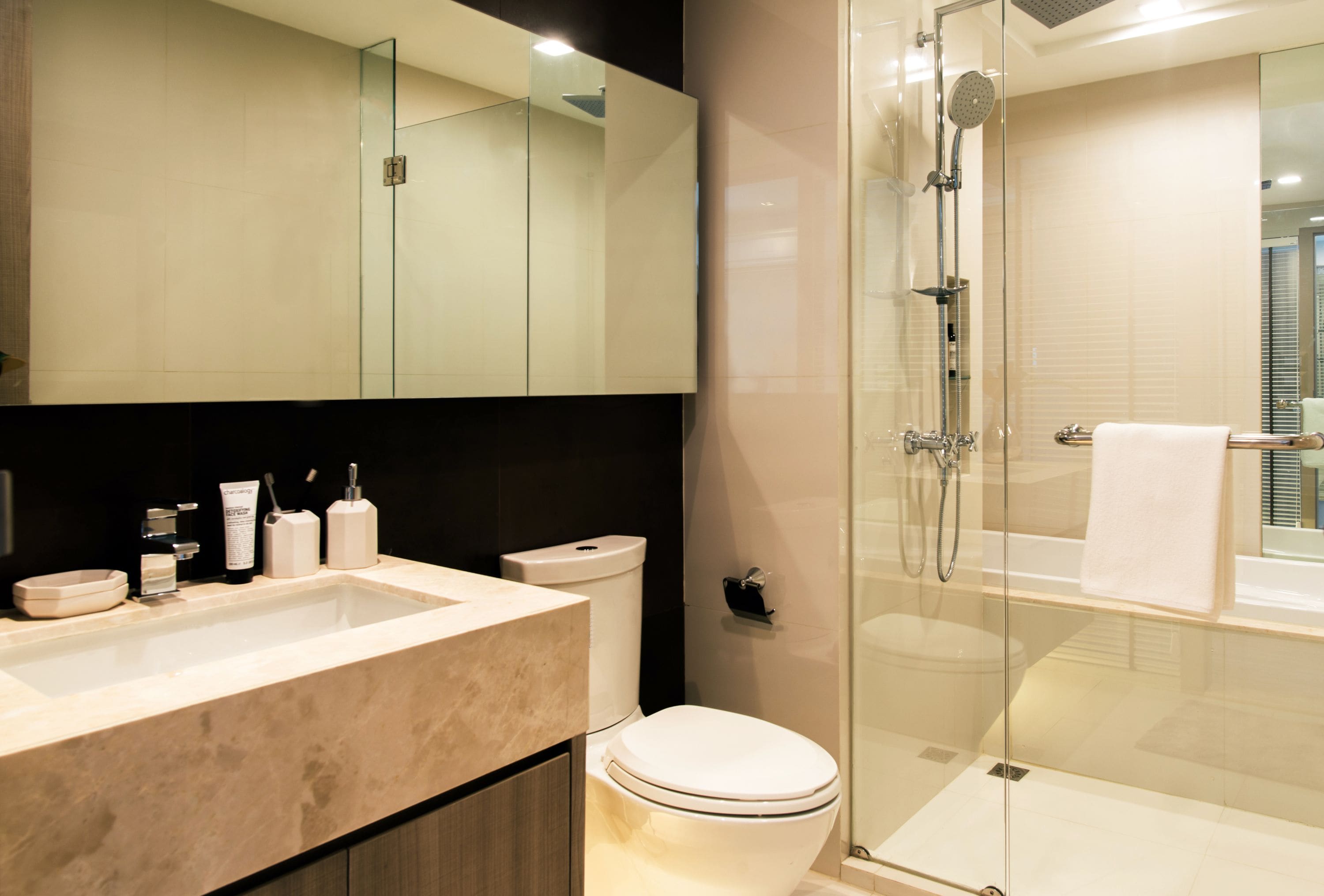 A modern bathroom with a glass shower enclosure, a large mirror, and a vanity with a sink and toiletries.