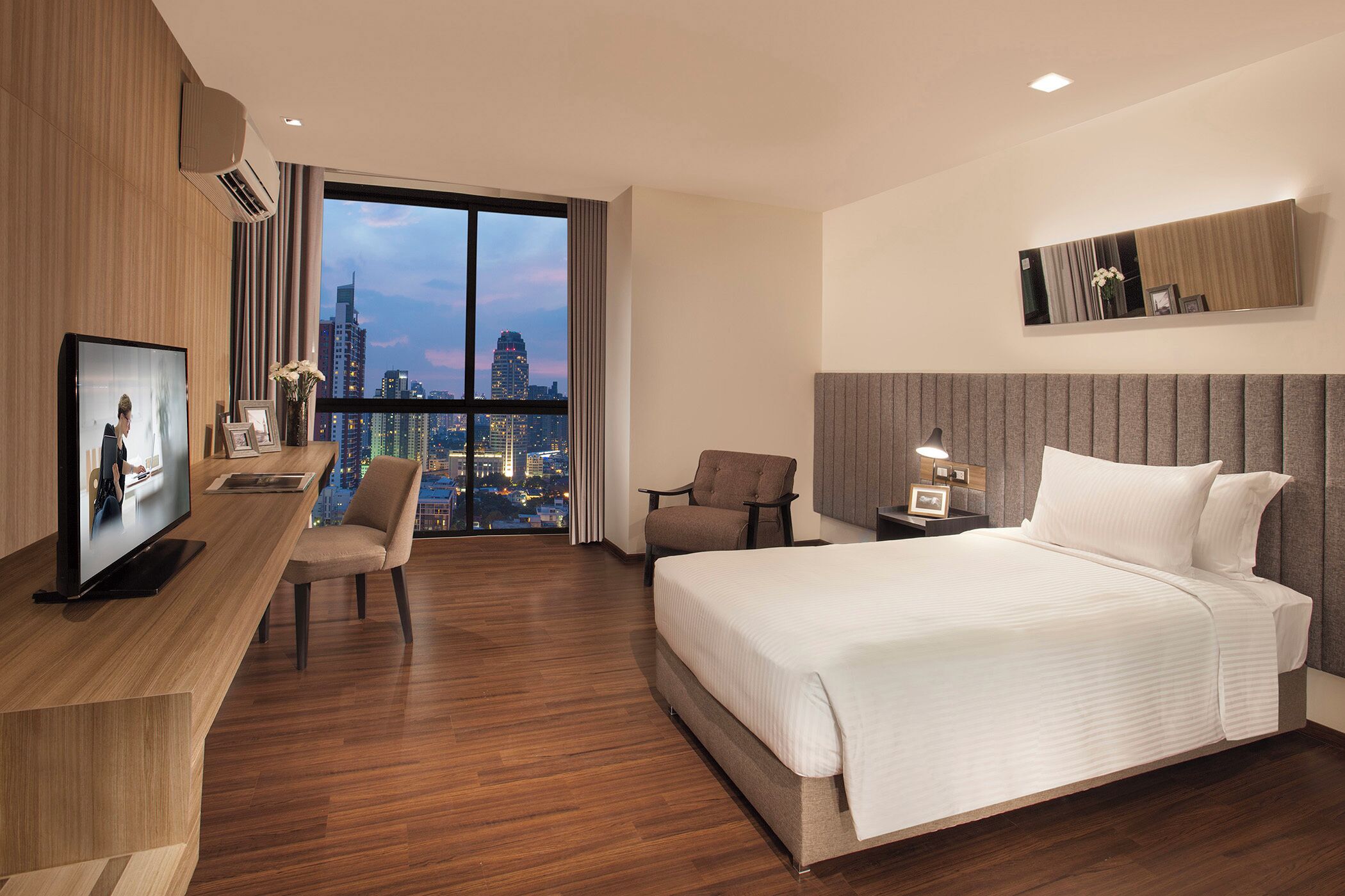Habitación de hotel con cama, escritorio con televisor, silla, mesita de noche y vista panorámica de la ciudad.