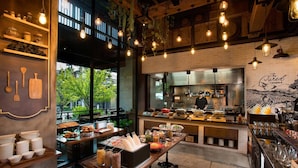 Un restaurant au décor rustique, avec des murs en briques apparentes, des poutres en bois et des lampes suspendues. On peut y voir différents comptoirs de restauration et un espace bar.