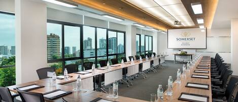A conference room with a long table, chairs, and a projector screen displaying "SOMERSET EKAMAI BANGKOK".