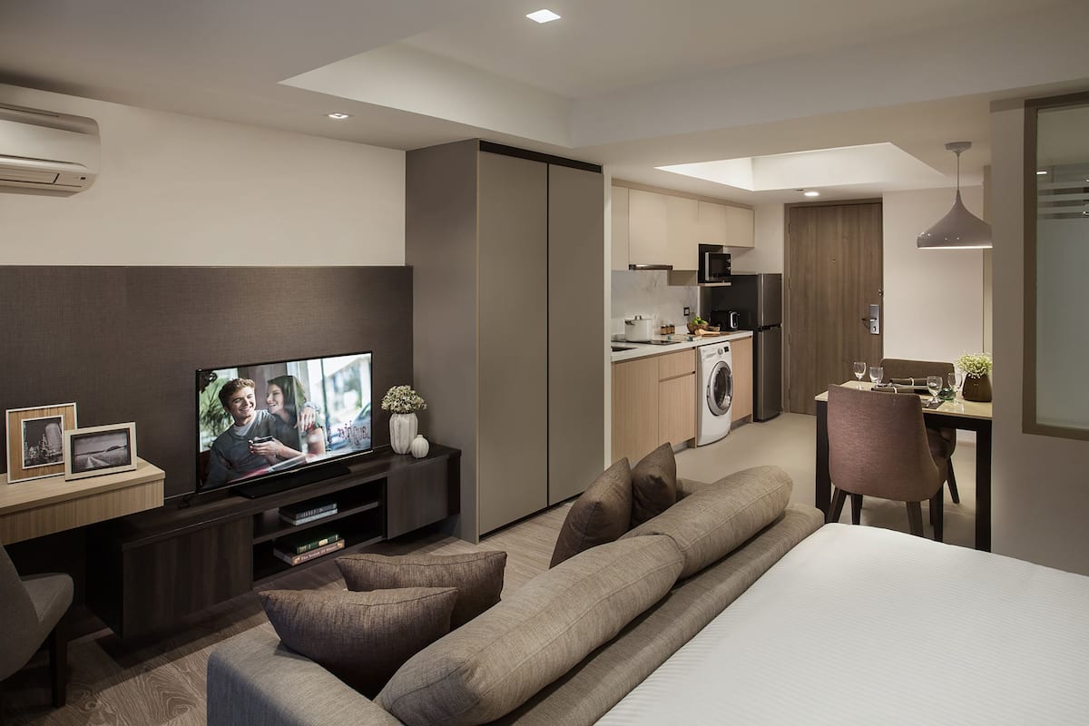 Una habitación de hotel moderna con sofá, televisor, zona de comedor y kitchenette.