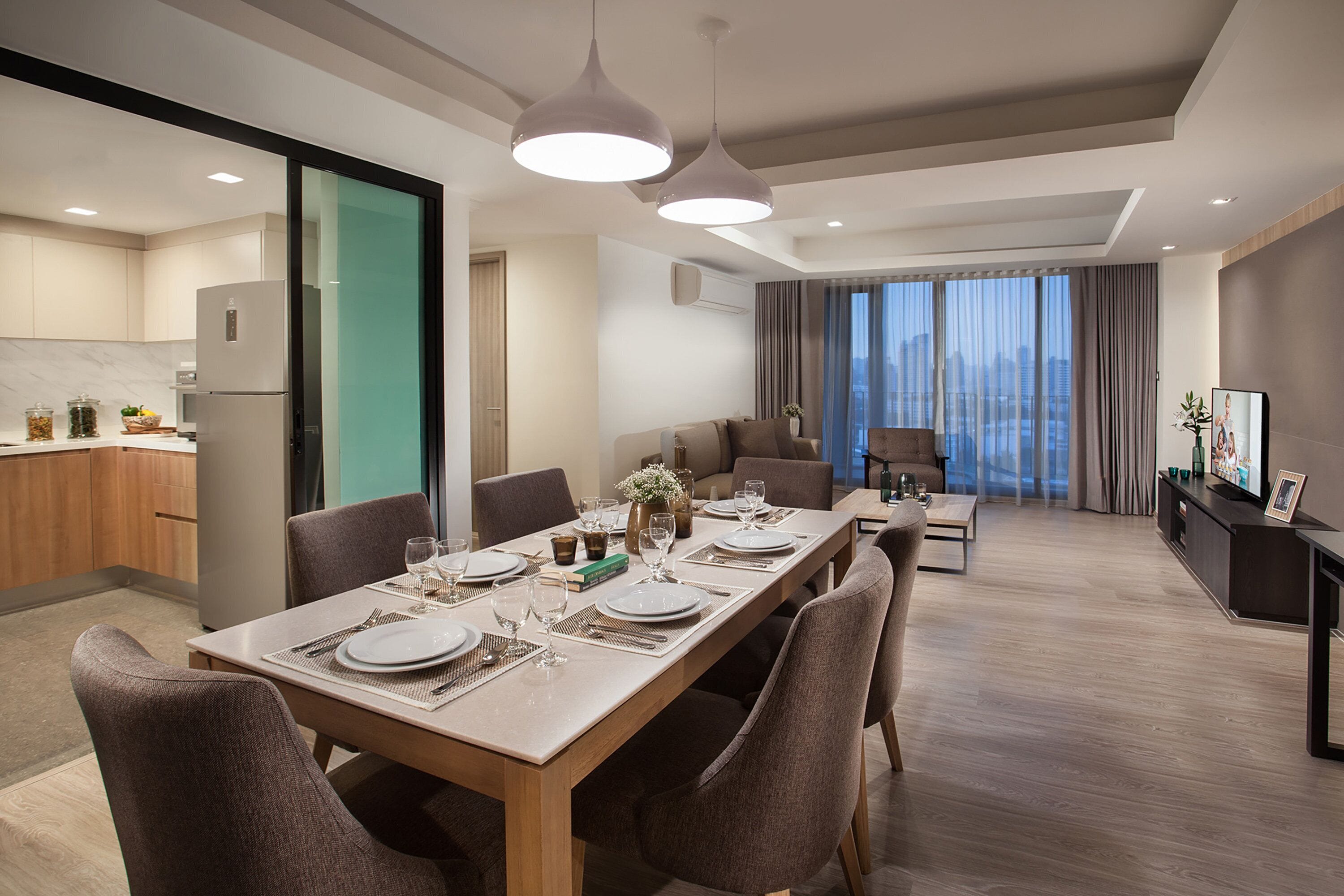 A modern dining area with a long table set for six, surrounded by chairs. A sofa and a small coffee table are visible in the background.