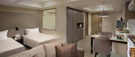 A modern hotel room with two beds, a sofa, a dining area, and a kitchenette.