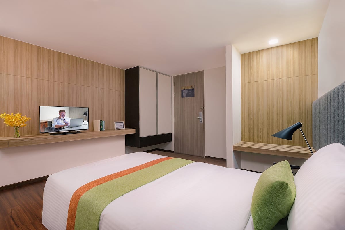 Habitación de hotel con cama, televisión en un estante, escritorio y ventana con lámpara.