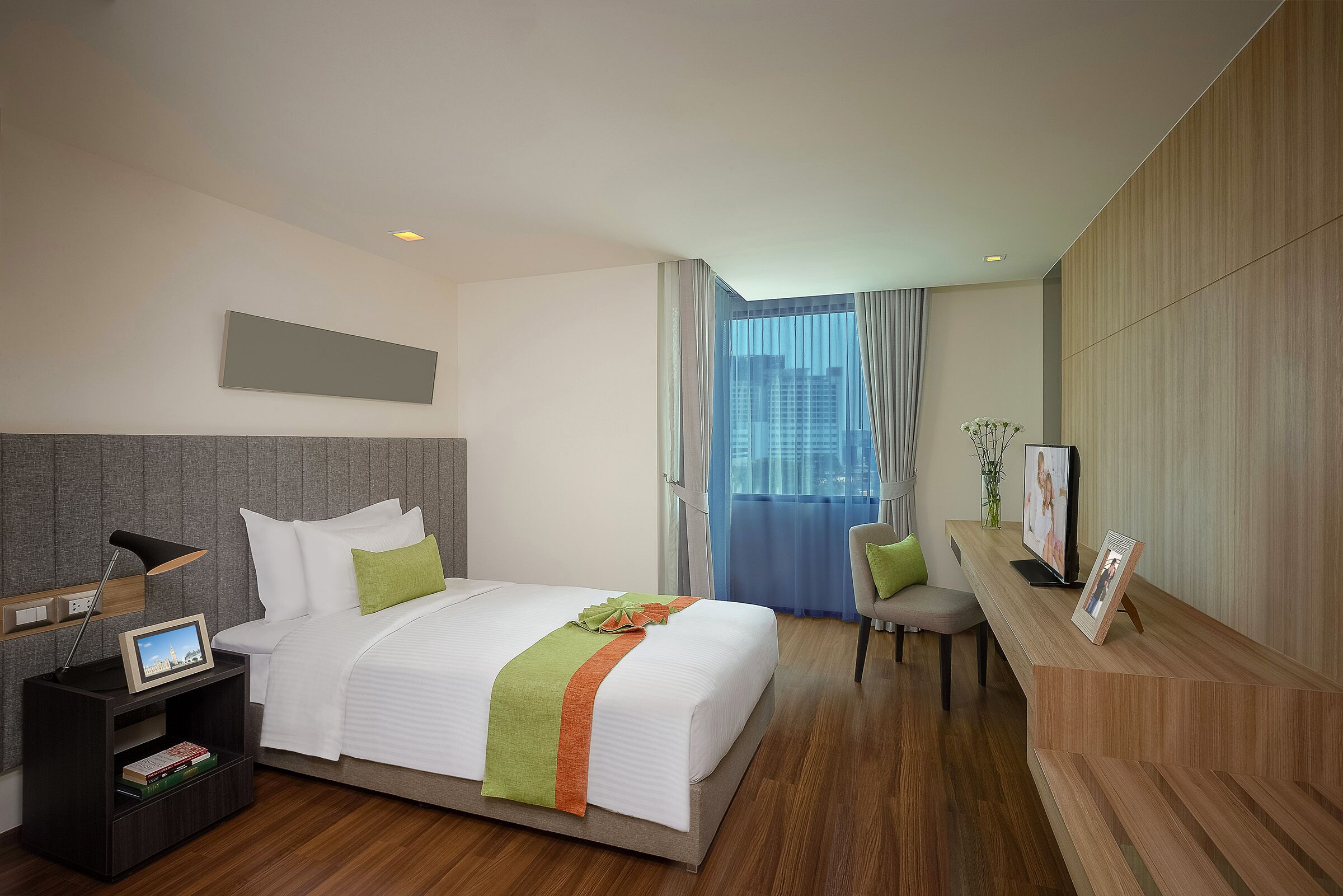 Une chambre d’hôtel avec un grand lit, un bureau avec un ordinateur, une chaise et une vue sur la ville par la fenêtre.