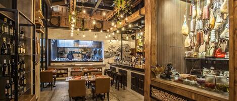 A restaurant with a bar area, wooden beams, hanging plants, and a variety of bottles on shelves.